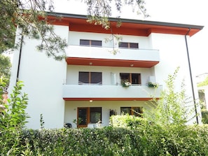 Un immeuble à plusieurs étages, doté d’une façade blanche, de balcons ornés de plantes et d’un toit rouge.