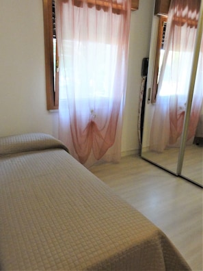 Une chambre avec un lit, un miroir et des rideaux légers.