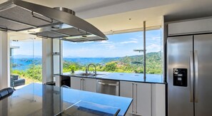 A modern kitchen with a large island, stainless steel appliances, and a view of a mountainous landscape.