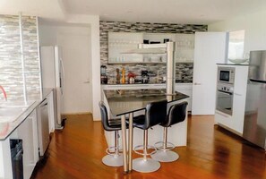 A modern kitchen with a central island, bar stools, and stainless steel appliances.