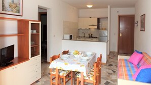 A compact living space with a dining area, kitchenette, and a bedroom with a colorful bed.