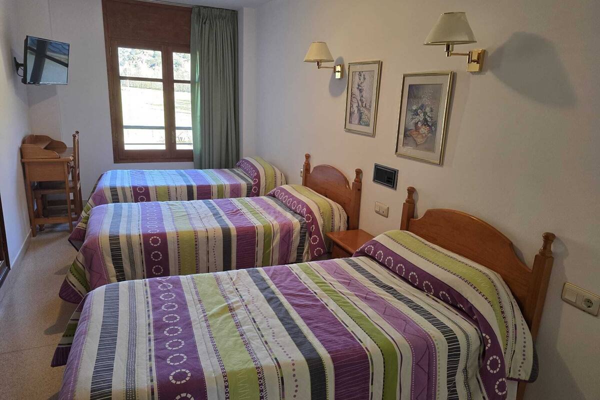 A hotel room with two beds, a desk, a TV, and a window with curtains.