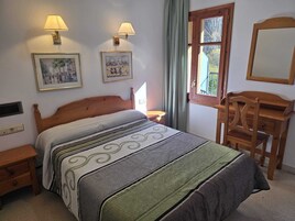 Un dormitorio con una cama, dos lámparas de pared, un aparador, una ventana con cortinas y dos cuadros en la pared.