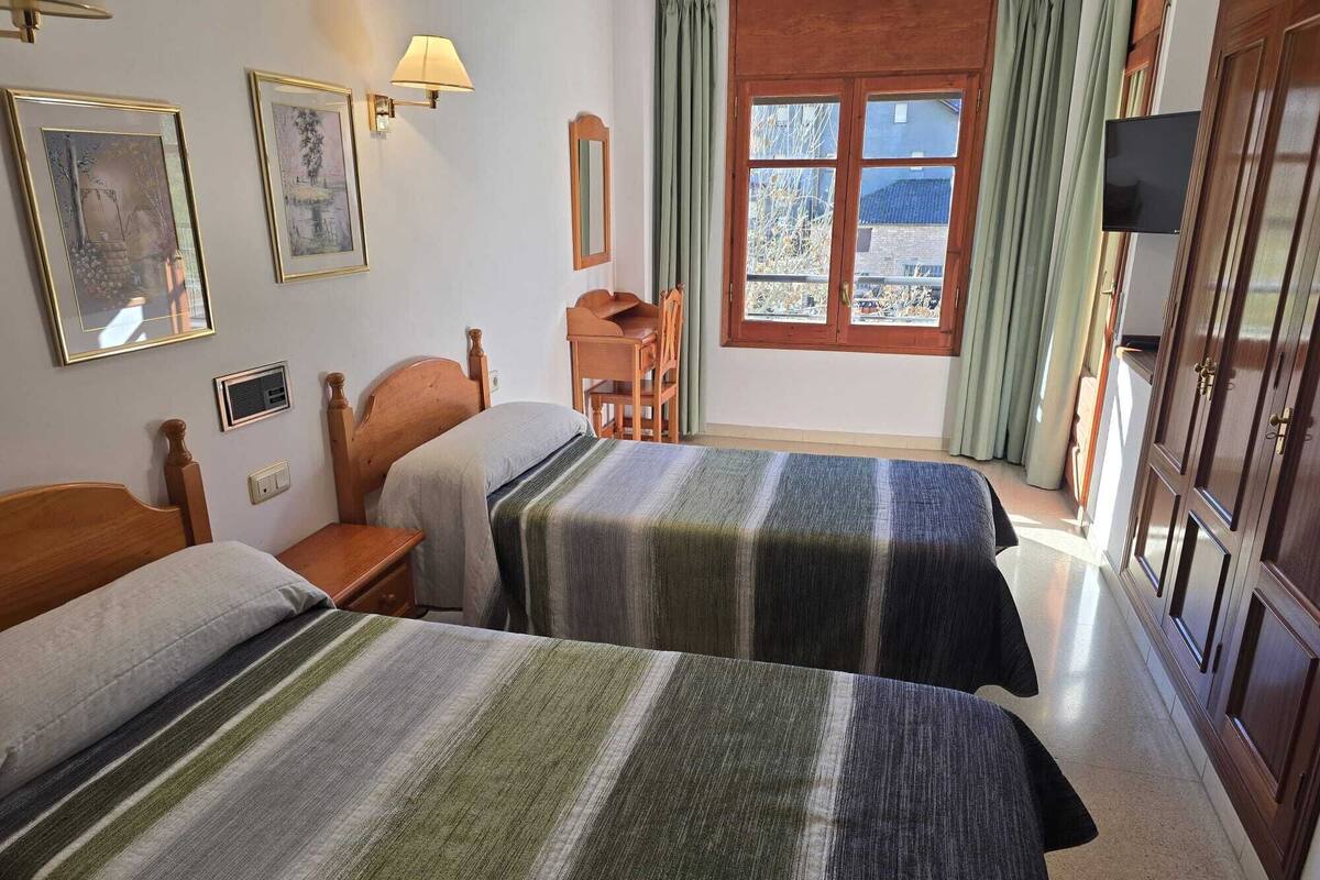 A room with two beds, a desk, a chair, a TV, and a window with curtains.