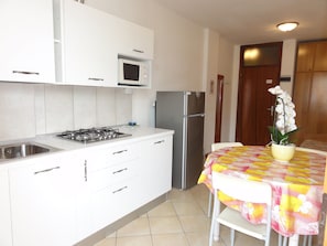 A kitchen with white cabinets, a gas stove, a microwave, and a refrigerator. There is a dining table with a floral tablecloth and a potted orchid. - Great Flat Close to the Beach (San Michele al Tagliamento)