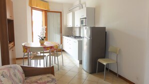 Une cuisine compacte équipée d’un réfrigérateur, d’un four à micro-ondes et d’une cuisinière. On y trouve également un coin repas avec une table et des chaises, ainsi qu’un lit recouvert d’une couvre-lit à motifs.