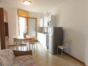A compact kitchen with a refrigerator, microwave, and stove. There is a dining table with chairs and a small potted plant. - Great Flat Close to the Beach (San Michele al Tagliamento)
