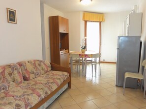 Una sala de estar con sofá, una mesa de comedor con sillas, una zona de cocina con refrigerador y una ventana con cortinas.