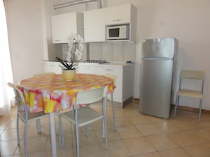 A compact kitchen with white cabinets, a microwave, a refrigerator, and a dining table with chairs. - Great Flat Close to the Beach (San Michele al Tagliamento)