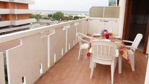 Ein Balkon mit Tisch für zwei Personen, weißen Plastikstühlen und Blick auf Strand und Meer.