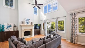 A spacious living room with a fireplace, a large sofa, and a ceiling fan. - Modern Vacation Home w/ Private Pool (Hilton Head Island)