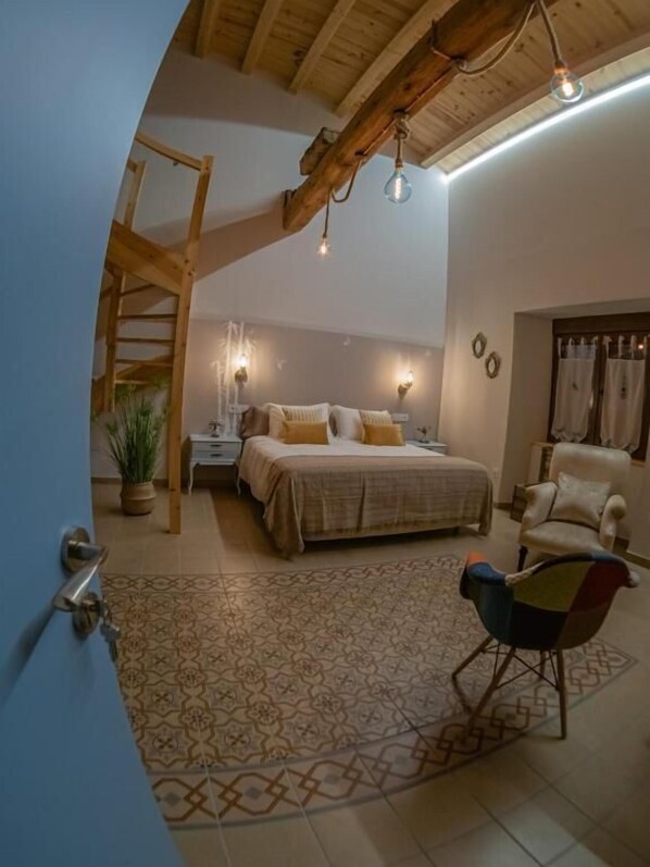 Un dormitorio con cama, una silla, una mesita de noche, una lámpara y una escalera.