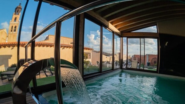 Un jacuzzi con caída de agua, ventanas amplias y vistas a un edificio con torre.