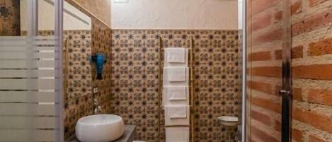 Une salle de bain avec un plafond en bois, un papier peint à motifs, un lavabo blanc et une cabine de douche en verre.