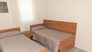 A room with two single beds, a nightstand with a lamp, and a window with curtains. - Villa Only 100mt From the Beach (San Michele al Tagliamento)