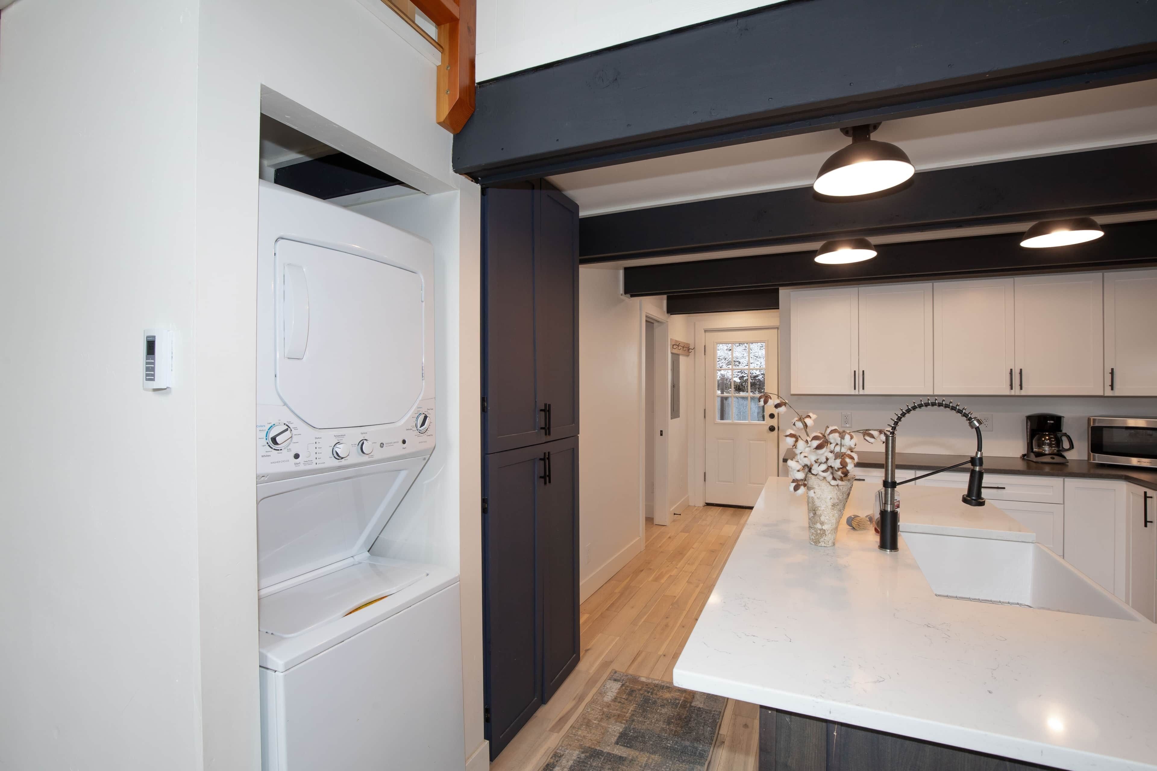 A modern kitchen with a built-in washer and dryer, a central island with a sink, and dark cabinetry.