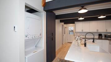 A modern kitchen with a built-in washer and dryer, a central island with a sink, and dark cabinetry.