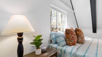 Ein Schlafzimmer mit einem Bett, einem Nachttisch mit Lampe, einer Zimmerpflanze und einem Fenster mit Aussicht.