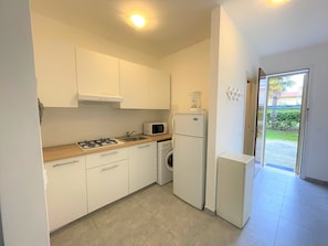Una cocina compacta con armarios blancos, cocina a gas, microondas, cafetera y lavadora.