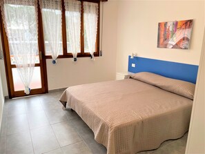 A bedroom with a bed, a nightstand, a wall-mounted lamp, and a window with curtains. - Bibione Modern Flat With Outdoor Space (San Michele al Tagliamento)