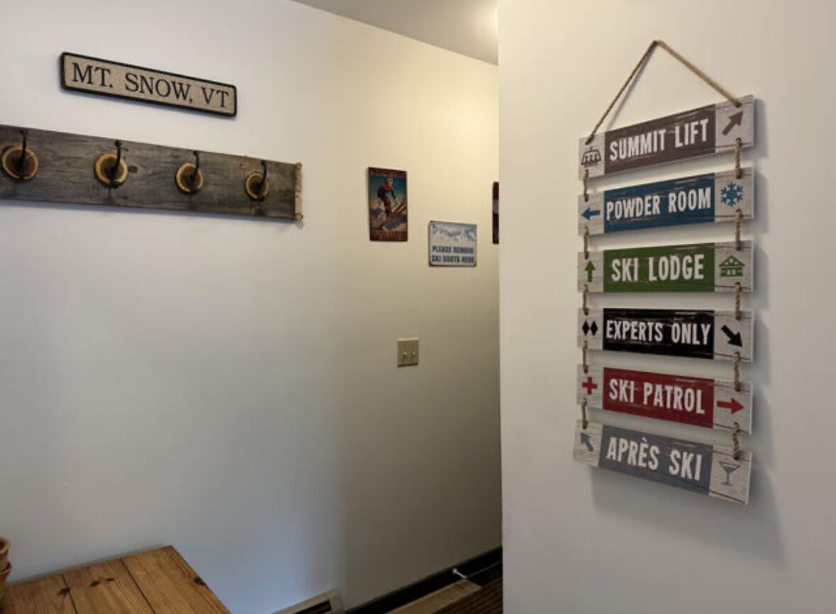 A hallway with a wooden coat rack, a sign reading "MT. SNOW, VT", and a wall-mounted signpost with ski-related directions.