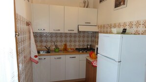 A compact kitchen with white cabinets, a stove, and a refrigerator. - Bibione House With Garden and Fireplace (San Michele al Tagliamento)