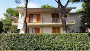 A two-story building with a balcony on the upper floor, surrounded by trees and a hedge. - Bibione House With Garden and Fireplace (San Michele al Tagliamento)