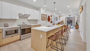 Een moderne keuken met witte kasten, roestvrijstalen apparatuur en een centraal eiland met barstoelen.