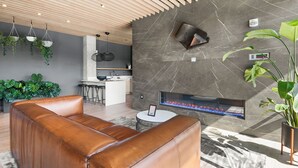 Een moderne woonkamer met een leren bank, een open haard en een keuken op de achtergrond.