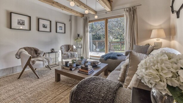 A living room with a sofa, armchair, and coffee table, a fireplace, and a large window with a view of trees. - Charming Chalet | 168m2 | 6 pax | Familial | View (Les Houches)