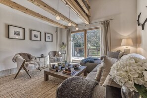 A living room with a sofa, armchair, and coffee table, a fireplace, and a large window with a view of trees. - Charming Chalet | 168m2 | 6 pax | Familial | View (Les Houches)