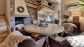A cozy living room with a stone fireplace, wooden beams, and a round wooden table surrounded by plush chairs. - Charming Chalet | 168m2 | 6 pax | Familial | View (Les Houches)