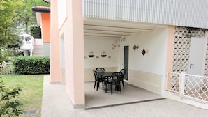 An outdoor patio area with a table and chairs, a covered walkway, and a decorative wall. - Bibione Apartment Near the Beach (San Michele al Tagliamento)