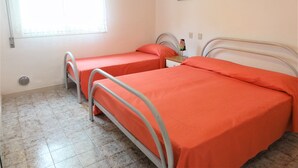 A room with two beds, a window with blinds, a radiator, and two framed pictures on the wall. - Bibione Apartment Near the Beach (San Michele al Tagliamento)