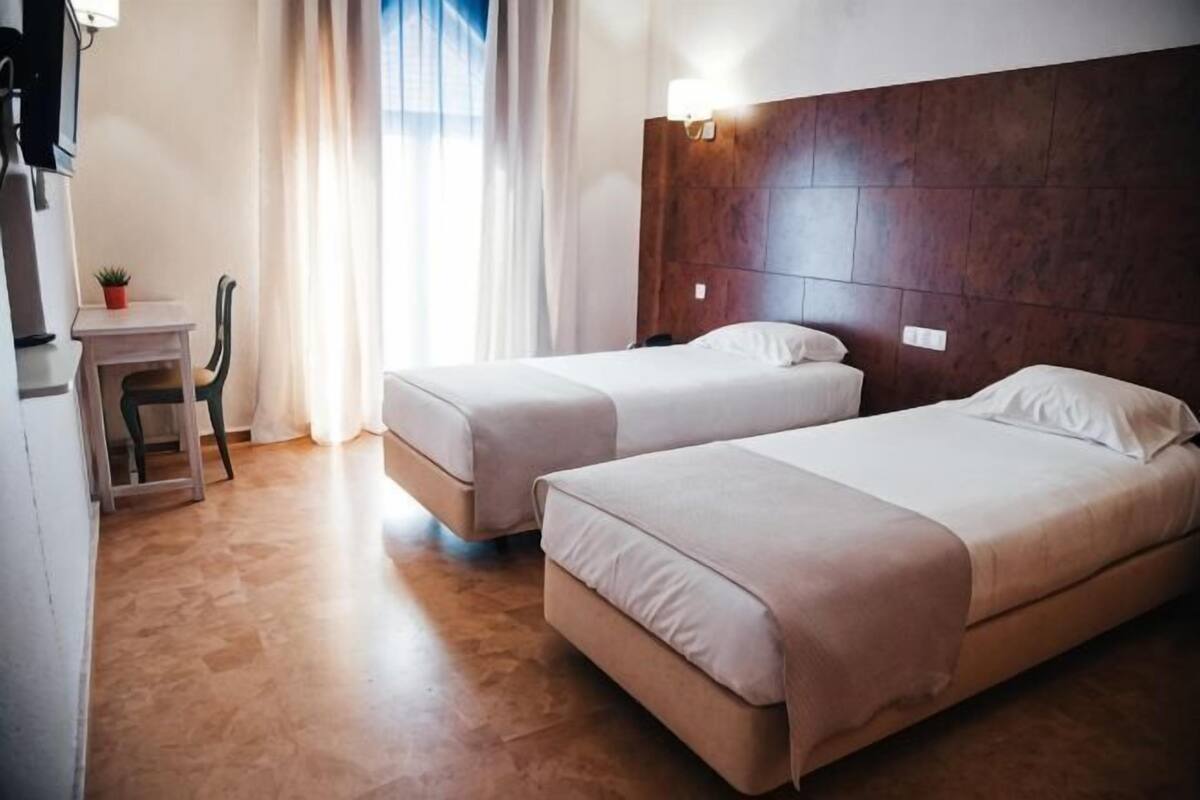 A hotel room with two beds, a desk, and a chair.