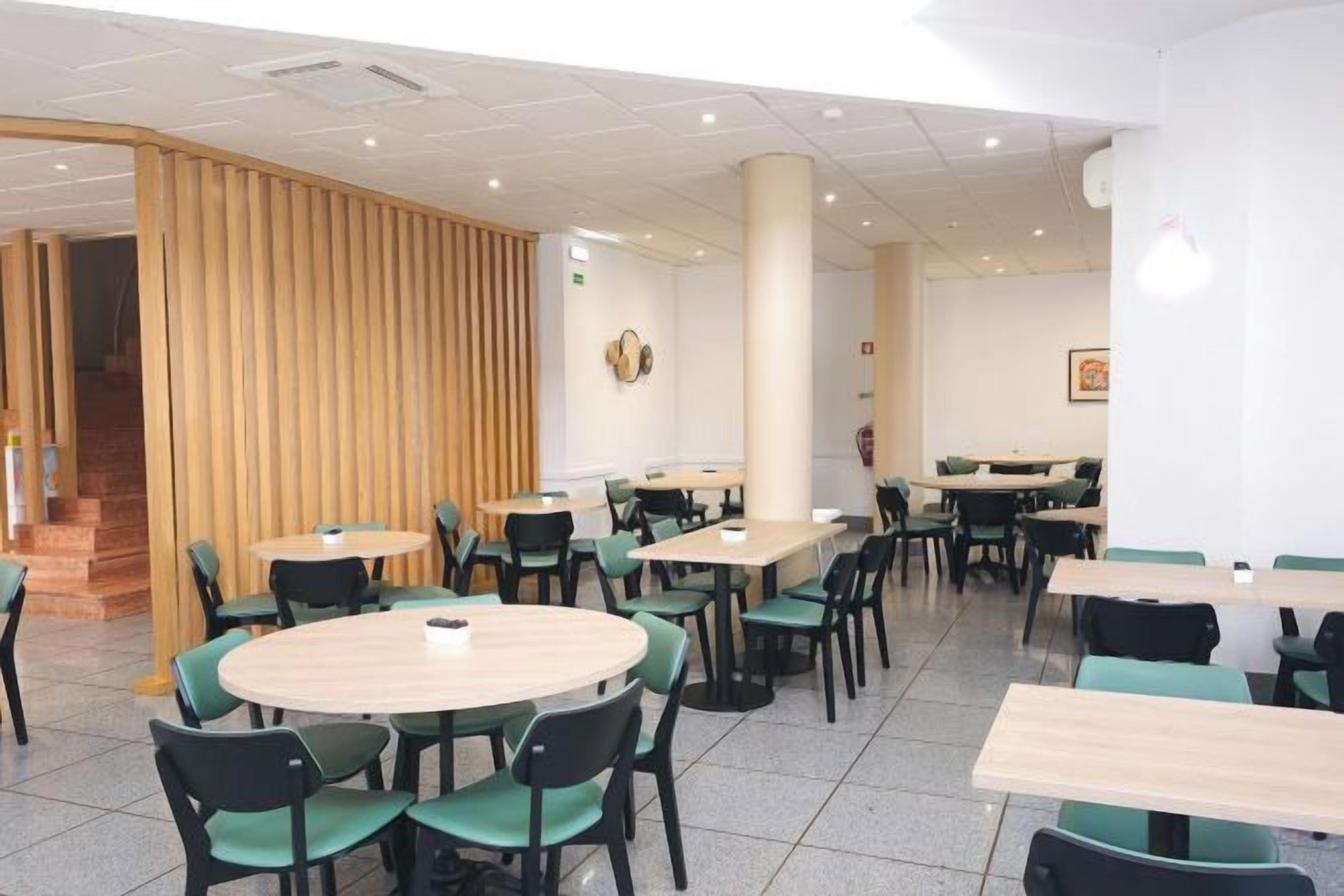Un área de comedor con mesas y sillas redondas, un separador de madera y una escalera.