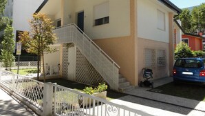 A two-story building with a white and beige exterior, a staircase, and a small garden area. - Bibione Flat With Terrace Near the sea (San Michele al Tagliamento)