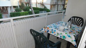 A balcony with a table and chairs, a white fence, and a building in the background.