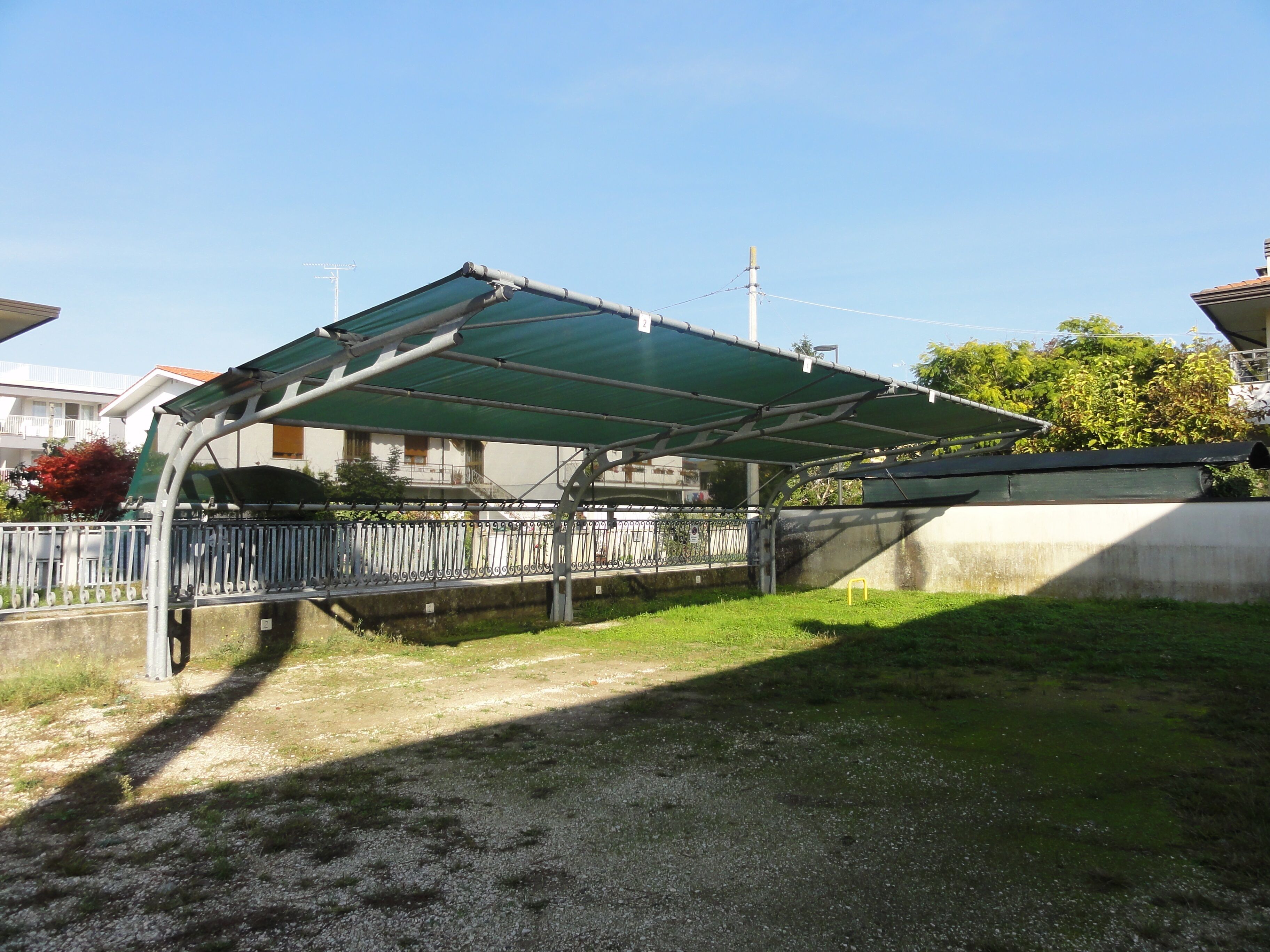 Un espace extérieur abrité, délimité par une clôture en métal, un mur en béton et un sol recouvert d’herbe.