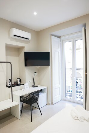 A modern hotel room with a white desk, black chair, and a large window.