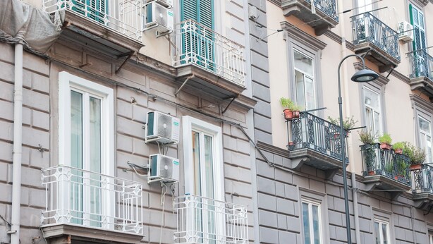 A multi-story building with balconies, air conditioning units, and potted plants.