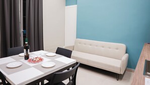 A dining area with a table set for four, a bottle of wine, and a bowl of snacks.