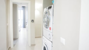 A laundry area with stacked washers and dryers, a hallway leading to a room with a door, and a light switch on the wall.
