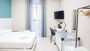 A hotel room with a bed, a desk, a chair, a bathtub, a TV, and a window with curtains.