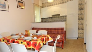 A dining area with a table set for four, white chairs, a red and yellow floral tablecloth, and a red plaid sofa. - Apartment in Villa With Fenced Garden (San Michele al Tagliamento)