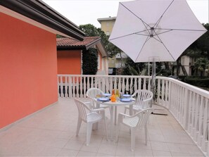 A balcony with a table and chairs, a white umbrella, and a white railing. - Apartment in Villa With Fenced Garden (San Michele al Tagliamento)