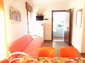 A room with a red sofa, two orange chairs, a television on a stand, and a painting on the wall.