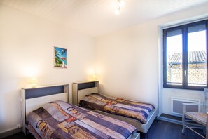Una habitación con dos camas, una silla, un ventanal y un cuadro en la pared.