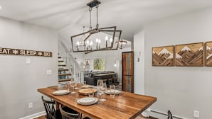 Un coin repas avec une table en bois dressée pour six personnes, des chaises noires et un lustre.
