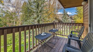 Une terrasse en bois avec deux tables et des chaises, donnant sur une cour verdoyante et des arbres.
